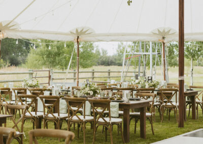 Tables and chairs set up under a tent rental with a checkerboard dance floor nearby